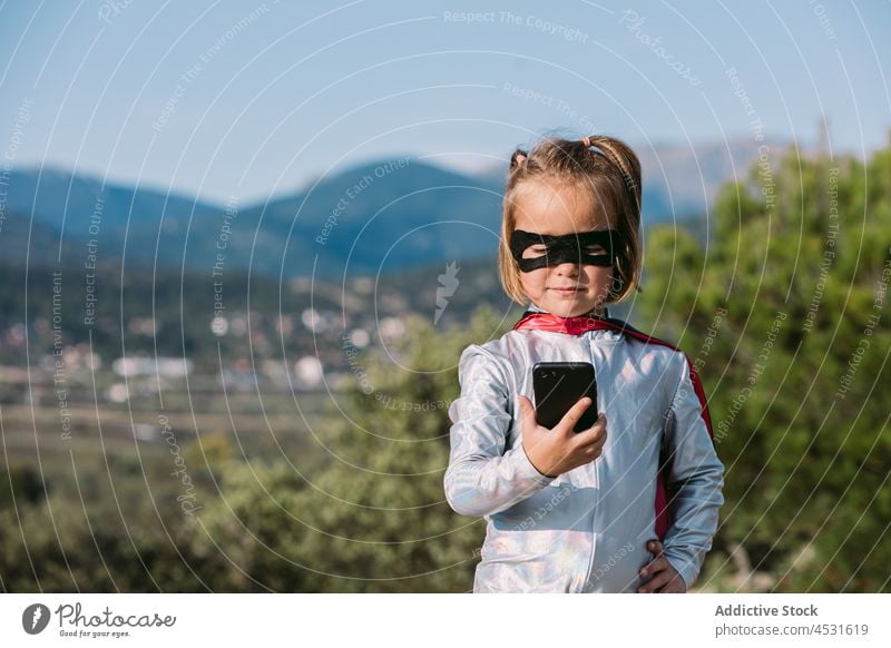 Tapferes Mädchen im Superheldenkostüm beim Surfen auf dem Smartphone Kind Mut benutzend Browsen Text Nachricht so tun, als ob Kraft selbstsicher selbstbewusst