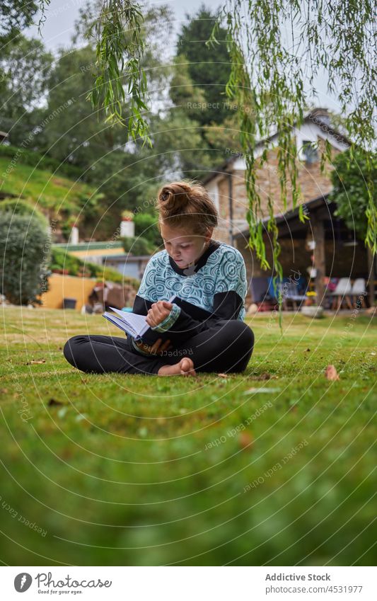 Mädchen liest Buch auf Rasen Kind lesen Landschaft Literatur Kindheit Zeitvertreib Hobby Hinterhof Freizeit wohnbedingt Hof Barfuß Haus Fokus Leseratte ruhen