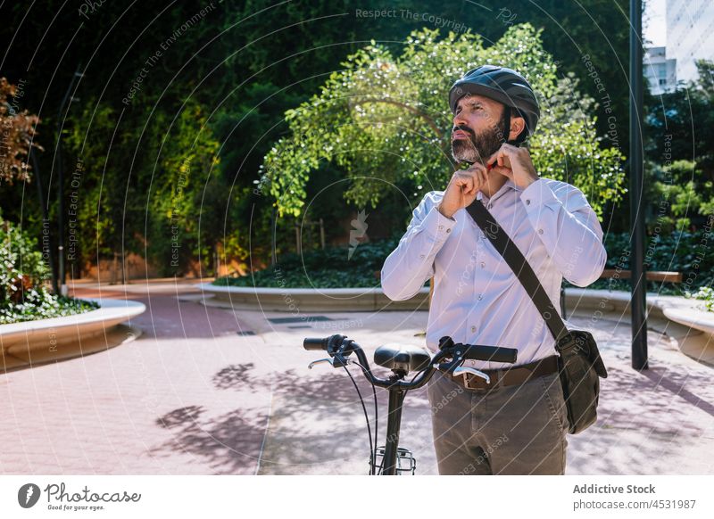 Männlicher Arbeiter, der sich vor dem Fahrradfahren einen Helm aufsetzt Mann befestigen Schutzhelm Park formal Mitarbeiter ernst Hobby ausrichten männlich