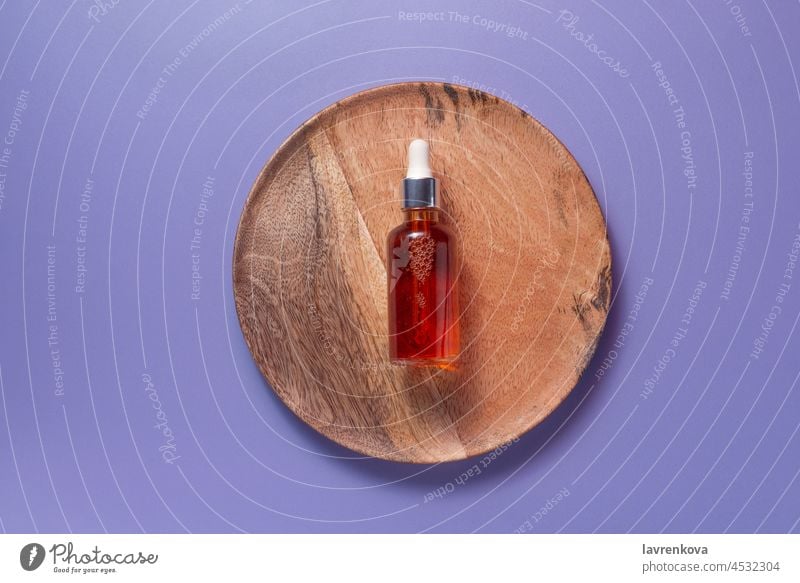 Natürliches organisches Vitamin-C-Serum auf einem Holzteller auf violettem Hintergrund, Erdöl Kosmetik Haut Pflege Flasche Schönheit Essenz Aufhellung Objekt