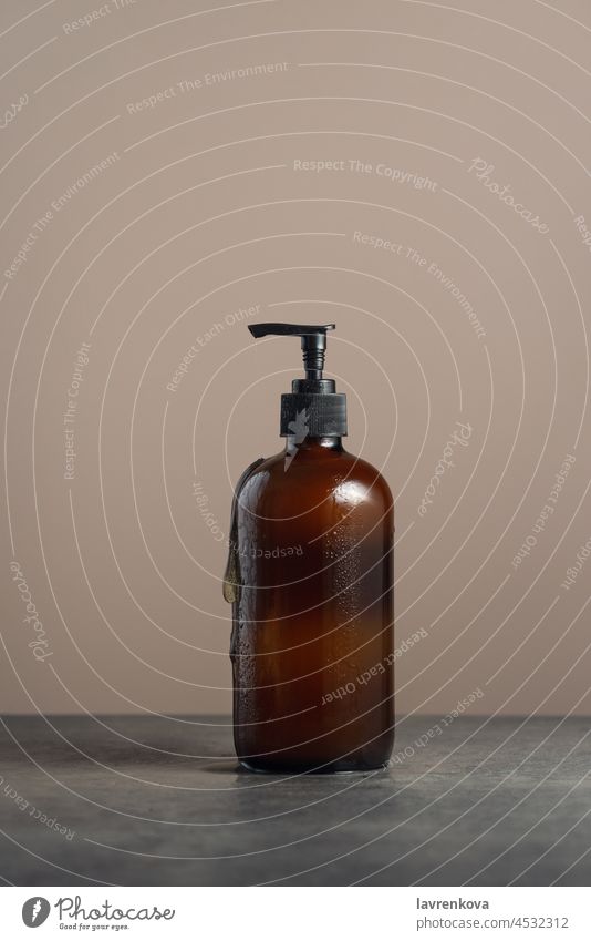 Umweltfreundlicher Braunglas-Seifenspender mit Pumpflasche, gefüllt mit Spülmittel oder Körperpflegemittel auf dunklem Marmorhintergrund bodywash Pflege