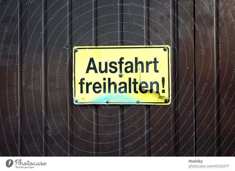 Kaputtes gelbes Ausfahrt freihalten Schild aus Plastik mit schwarzer Schrift auf braunen Holztor im Nordend von Frankfurt am Main in Hessen Kunststoff kaputt