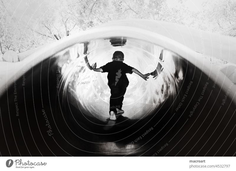 Kind in einer Rutsche rutsche röhre metallröhre spiegelnd steil glatt spielplatz kindheit rücken stehend groß freude klettern glückliche kindheit schwarz weiß