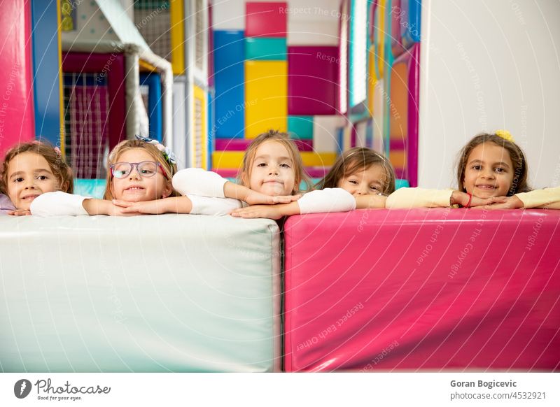 Gruppe niedlicher kleiner Mädchen, die sich hinter großen Lederblöcken verstecken Glück Menschengruppe Lächeln Freunde Vorschule Kind wenig Kindergarten