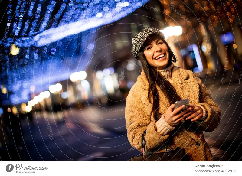 Hübsche junge Frau benutzt ihr Handy auf der Straße zur Weihnachtszeit Tasche schön Browsen Verschlussdeckel Funktelefon Weihnachten Großstadt Stadtbild