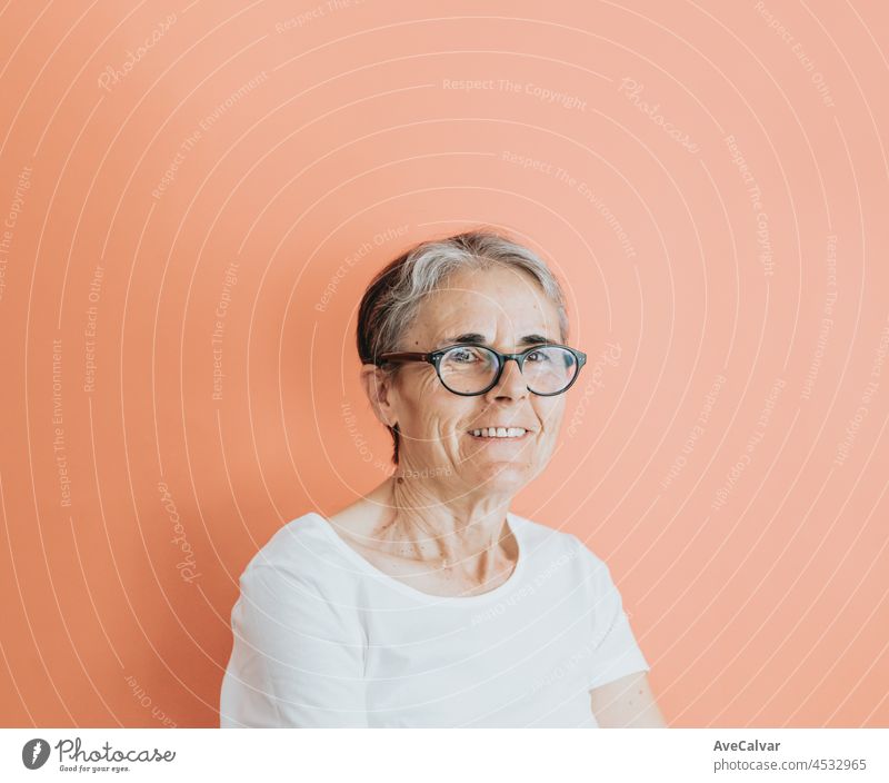 Alte Frau tut lächelnd in die Kamera, Kopie Raum, weiche orange abnehmbaren Hintergrund, minimale grundlegende, alte Menschen Lebensstil, Anzeigenkonzept Deal, weißes Hemd Raum