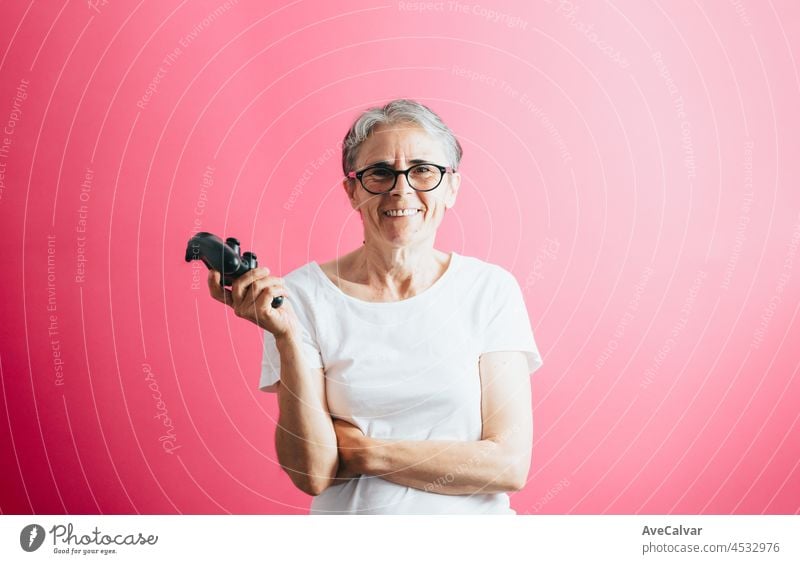 Alte ältere Frau lächelnd in die Kamera, während sie eine Konsole Pad, Videospiele spielen pastellrosa abnehmbaren Hintergrund, Videospiele alte Menschen, Kopie Raum, weißes Hemd Raum