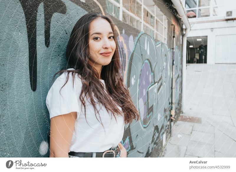 Porträt der jungen arabischen Frau trägt weißes Hemd und blaue Jeans lächelnd in die Kamera auf einer Backsteinmauer mit Graffiti-Malerei Hintergrund. Straße Leben Stil, cool trendy. Soziales Netzwerk Konzept