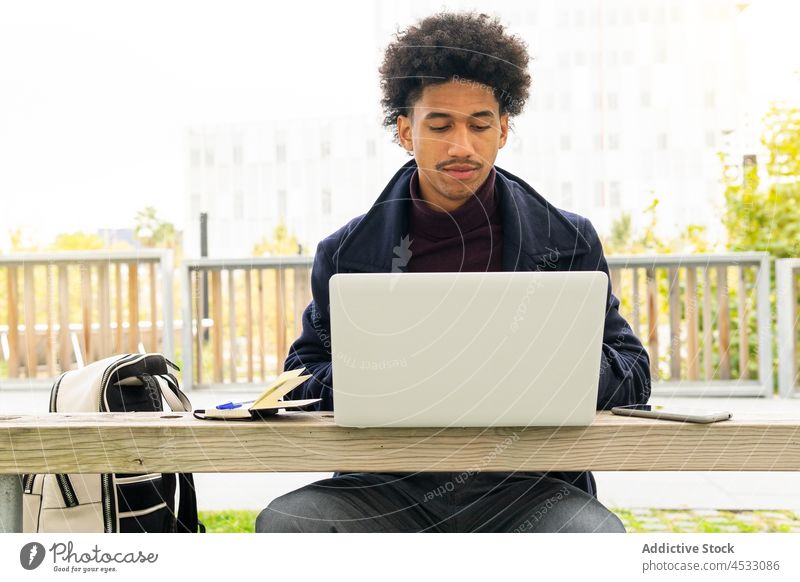 Schwarzer Mann benutzt Laptop im Park freiberuflich benutzend online Internet Fokus männlich Bank Arbeit Browsen Konzentration Netbook selbständig Surfen