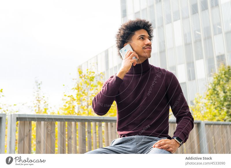 Schwarzer Mann telefoniert mit Smartphone auf einer Bank sitzend benutzend Telefonanruf prüfen Park sprechen online zuschauen reden ernst männlich Apparatur