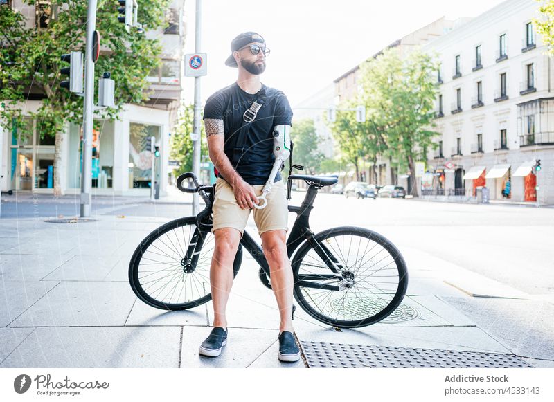 Mann mit Armprothese steht in der Nähe eines Fahrrads in der Stadt Arme Prothesen Prothetik künstlich Glied Amputierte Bionik Straße männlich Hipster cool