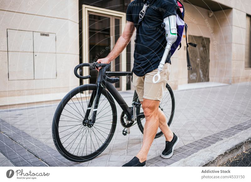 Anonymer Mann mit Armprothese geht mit Fahrrad auf der Straße Prothesen Arme Amputierte künstlich Glied Bionik Großstadt männlich Handicap Hipster schlendern