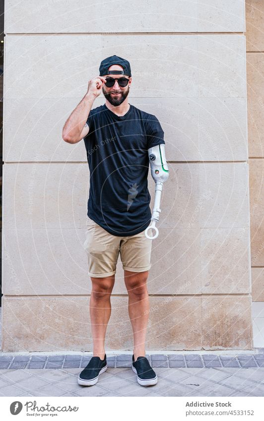 Lächelnder Hipster mit Armprothese in der Stadt Mann Prothesen Arme künstlich Glied Bionik Metall cool Großstadt männlich Inhalt Handicap Wand fettarm Straße