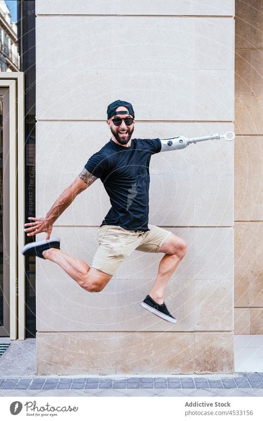 Energetischer Mann mit Armprothese springt in der Stadt künstlich Arme Prothesen springen Glück Straße sorgenfrei Amputierte Bionik männlich Hipster Handicap