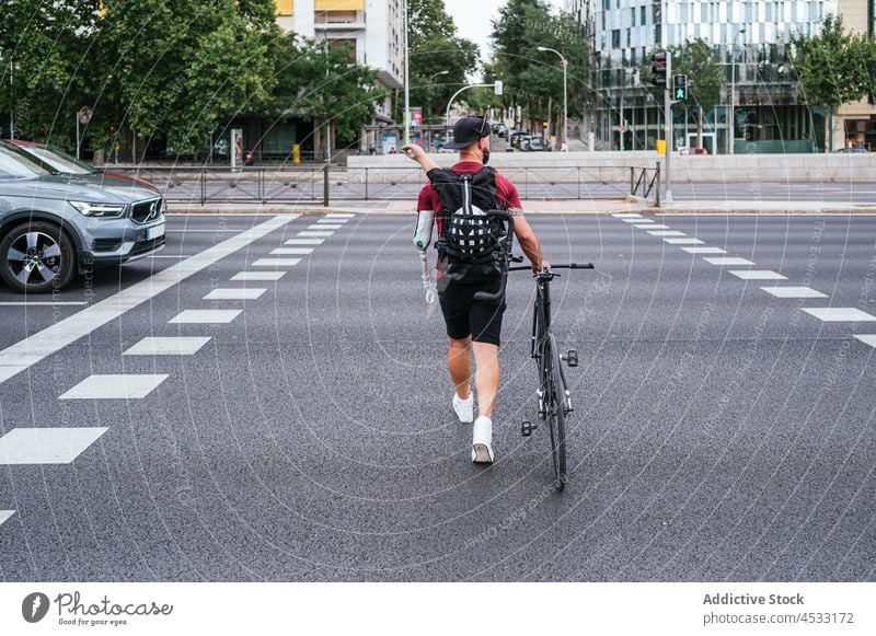 Anonymer Mann mit Armprothese geht mit Fahrrad am Straßenrand spazieren Prothesen Arme Zebrastreifen Amputierte künstlich Glied Bionik Großstadt Spaziergang