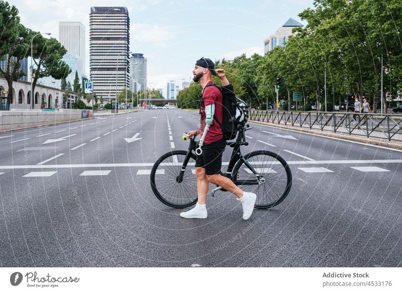 Mann mit Armprothese geht mit Fahrrad am Straßenrand spazieren Prothesen Arme Zebrastreifen Amputierte künstlich Glied Bionik Großstadt Spaziergang männlich