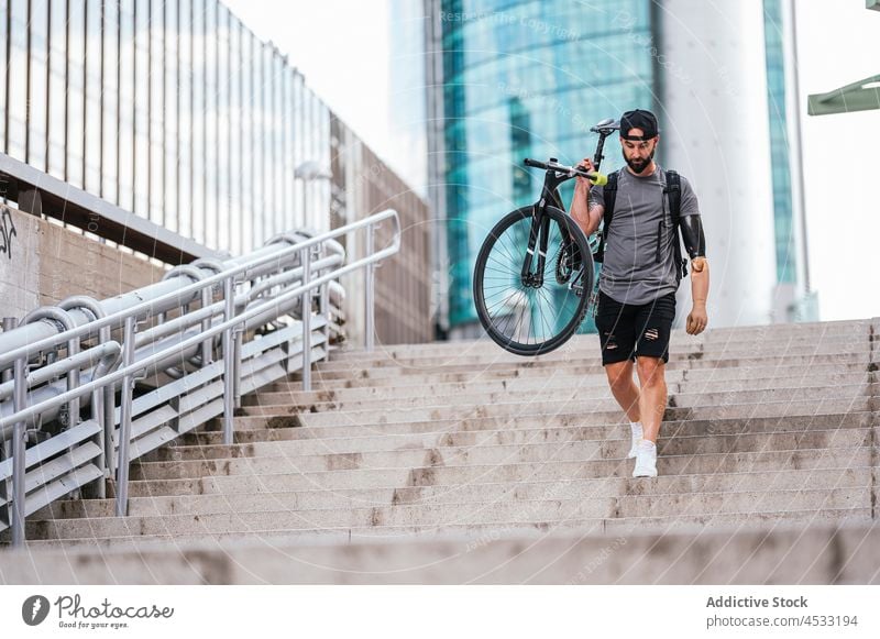 Mann mit Armprothese geht mit Fahrrad die Treppe hinunter künstlich Prothesen Arme Großstadt Amputierte Hipster im unteren Stockwerk männlich Handicap