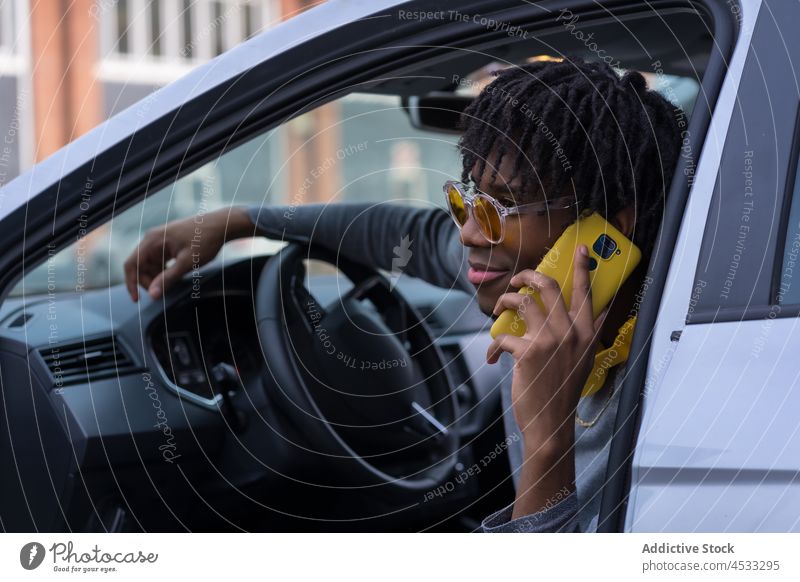 Schwarzer männlicher Fahrer, der im Auto mit seinem Smartphone spricht Mann PKW offen benutzend Streetstyle cool Telefonanruf Stil Kommunizieren Anschluss Gerät