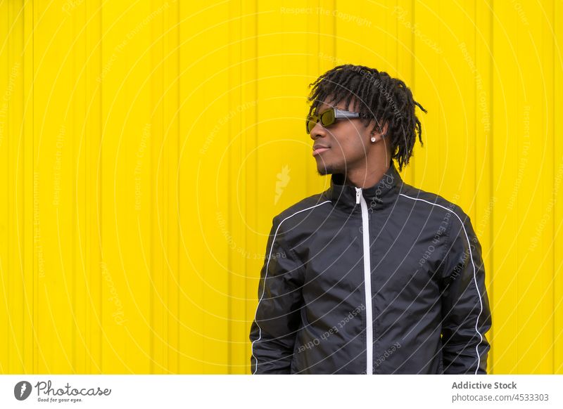 Lächelnder schwarzer Mann mit Sonnenbrille in der Nähe einer gelben Wand ausrichten cool Streetstyle positiv hell Stil trendy Vorschein Accessoire männlich