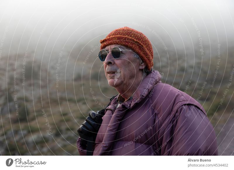 Ein Bergsteiger, ein älterer erwachsener Mann in den 70ern, der eine Daunenjacke, Handschuhe und eine Sonnenbrille trägt, genießt die Landschaft während einer Bergwanderung, Pyrenäen, Spanien