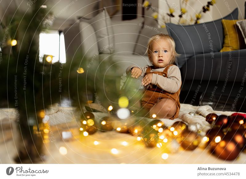 Lifestyle-Porträt von niedlichen kaukasischen Baby ein Jahr alt spielen mit Tannenbaum auf dem Boden zu Hause. Frohe Weihnachten und ein gutes neues Jahr 2022