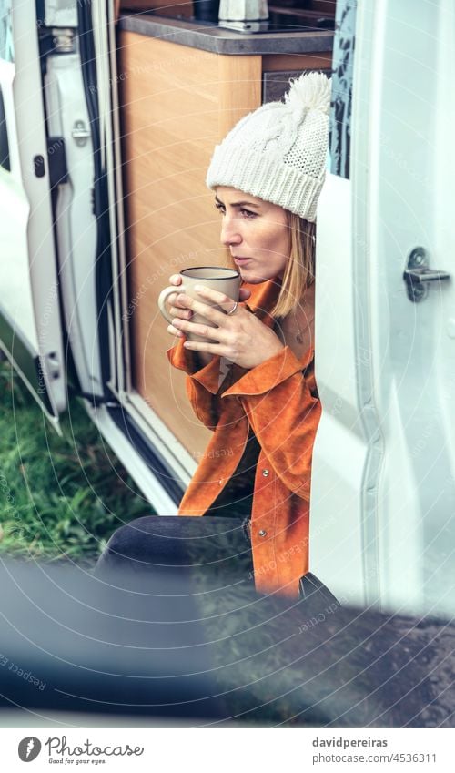 Frau trinkt Kaffee an der Tür eines Wohnmobils Sitzen Kleintransporter Winter Beteiligung Tasse blasend heiß Textfreiraum kalt nachdenklich Morgen ernst