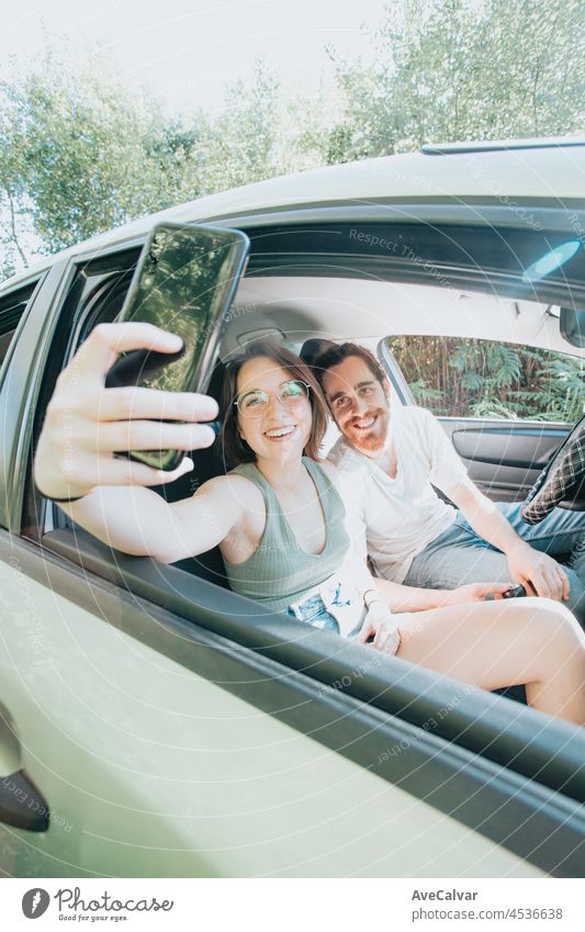 Schönes junges Paar, das eine Autoreise unternimmt. Autoreise, Frontalporträt lächelnd. Sie machen eine Pause vom Fahren und nehmen ein Selfie mit ihrem Telefon. Hipster modernes Paar.