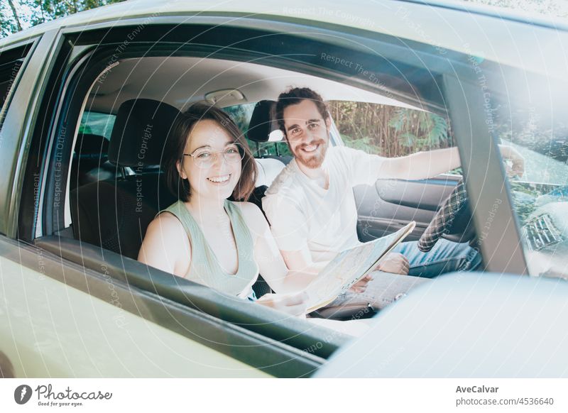 Schönes junges Paar auf einer Autoreise im Auto. Road Travel, frontal Porträt lächelnd. Sie nehmen eine Pause vom Fahren und suchen oder überprüfen Sie die Karte, um die Route zu sehen. Hipster modernes Paar.