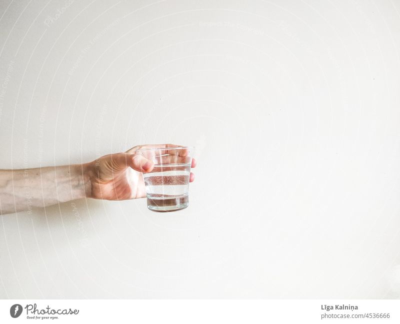 Hand, die ein Wasserglas mit negativem Raum hält minimalistisch sehr wenige Hintergrund Minimalismus einfach grau weiß Körperteil Finger Handgelenk Arme Mensch