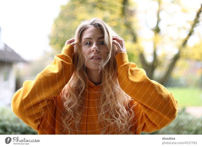 Portrait einer jungen, schlanken Frau mit langen, blonden Haaren und gelben Kapuzenpullover auf dem Balkon im Herbst junge Frau groß langhaarig schön anmutig