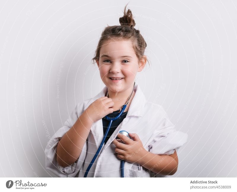 Fröhliches Mädchen im Arzt-Outfit Stethoskop Verkleidung spielen medizinisch spielerisch Kindheit Sanitäter Instrument heiter Glück positiv Atelier Brille