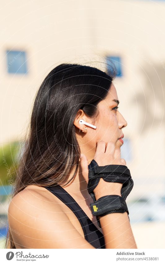 Frau in Sportkleidung hört Musik mit Ohrstöpseln Rollschuhläuferin zuhören Kopfhörer Sicherheit Handschuh behüten verhindern Training Gerät Athlet üben tws