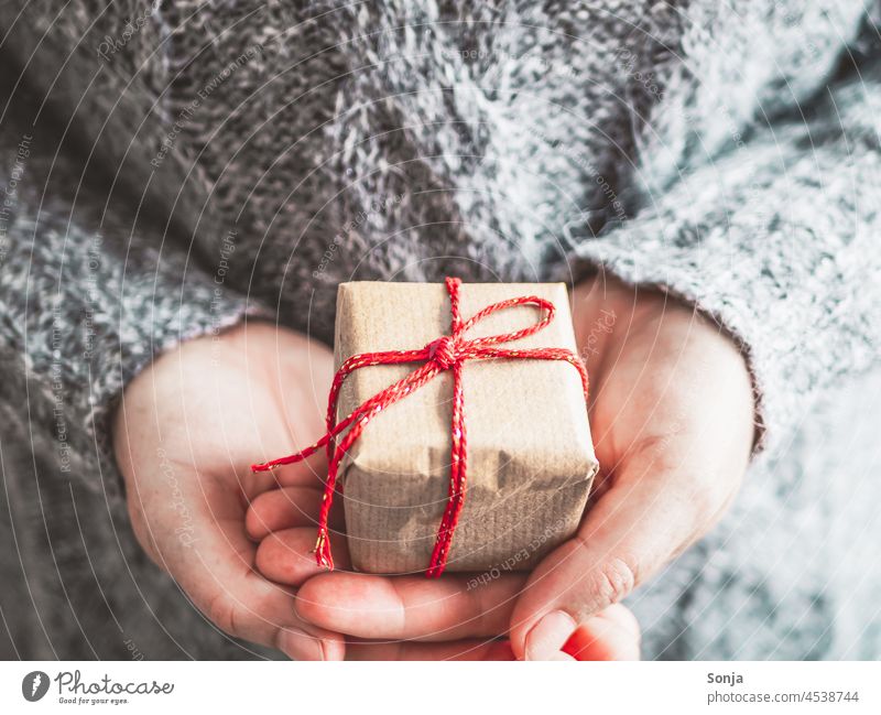 Frau hält ein Geschenkpaket mit roter Schleife in den Händen Paket Weihnachten verrotten Haende halten Winter Pullover grau geburtstag Lifestyle teilabschnitt