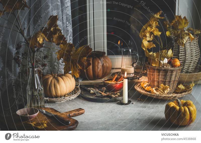 Gemütliche Herbst Küche Hintergrund mit Kürbissen, Herbstblätter, Kerzen, Schneidebrett und Küchenutensilien auf grauem Beton Tisch am Fenster. Häusliches Stillleben. Vorderansicht.