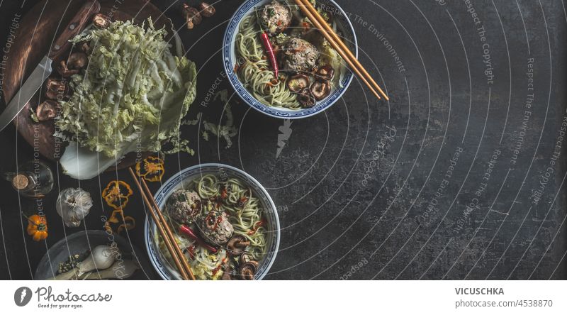 Schalen mit asiatischer Suppe mit Nudeln, Kohl, Pilzen, Shiitake, Knoblauch, Chili und Knödel in traditionellem Geschirr mit Stäbchen auf dunklem Betontisch. Food-Banner mit gesunden Ramen-Nudeln. Ansicht von oben