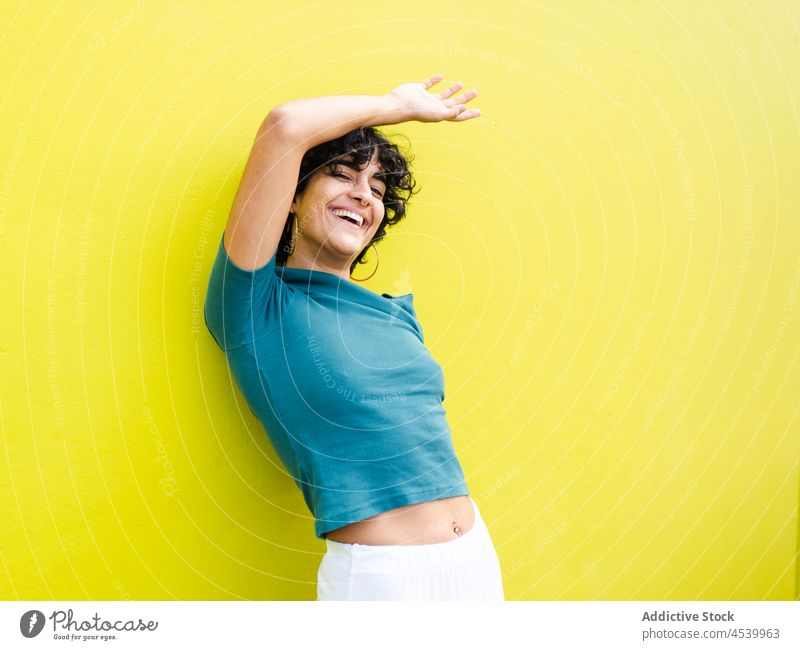 Fröhliche Frau mit erhobener Hand am Kopf in der Nähe einer hellen Wand Lachen Freude heiter froh lebhaft Körperhaltung Individualität expressiv Glee positiv