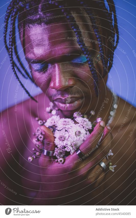 Ernster schwarzer Mann ohne Hemd mit Make-up und Blumen alternativ provokant exzentrisch Vorschein Blumenstrauß extravagant informell geblümt Pflanze