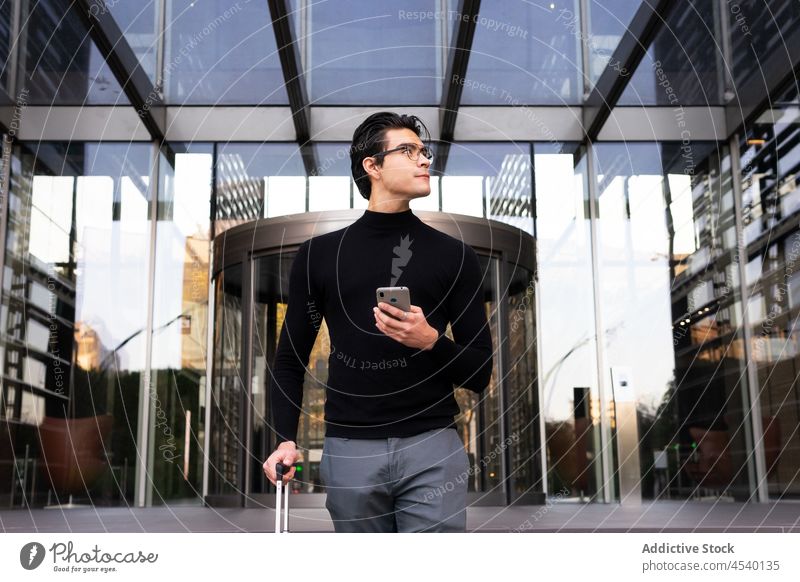 Asiatischer Geschäftsmann mit Koffer, der auf seinem Smartphone surft Mann Browsen online Straße Großstadt Unternehmer Ausflug Business Gebäude Anschluss modern
