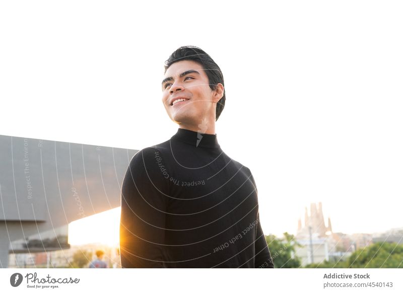 Seriöser asiatischer Mann auf sonniger Straße Gebäude Lächeln Großstadt Stil urban modern Vorschein Glück Sonnenlicht Outfit Freude ethnisch froh Bekleidung