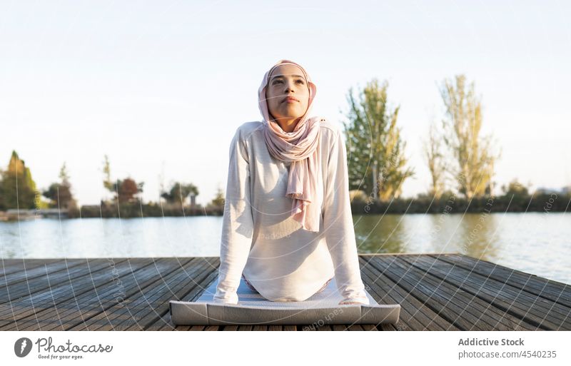 Friedliche arabische Frau beim Yoga am Deich Asana Stauanlage Hafengebiet Fluss üben Übung Gesunder Lebensstil Wasser muslimisch Kopftuch Hijab Ufer Achtsamkeit