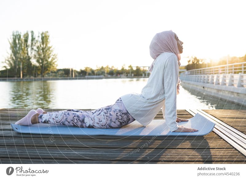 Friedliche arabische Frau beim Yoga am Deich Asana Stauanlage Hafengebiet Fluss üben Übung Gesunder Lebensstil Wasser muslimisch Kopftuch Hijab Ufer Achtsamkeit