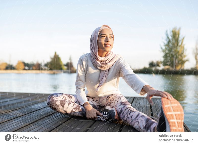 Positive arabische Frau bei Dehnungsübungen an der Böschung Aufwärmen Stauanlage Hafengebiet Fluss üben Übung Gesunder Lebensstil Sport sportlich Training