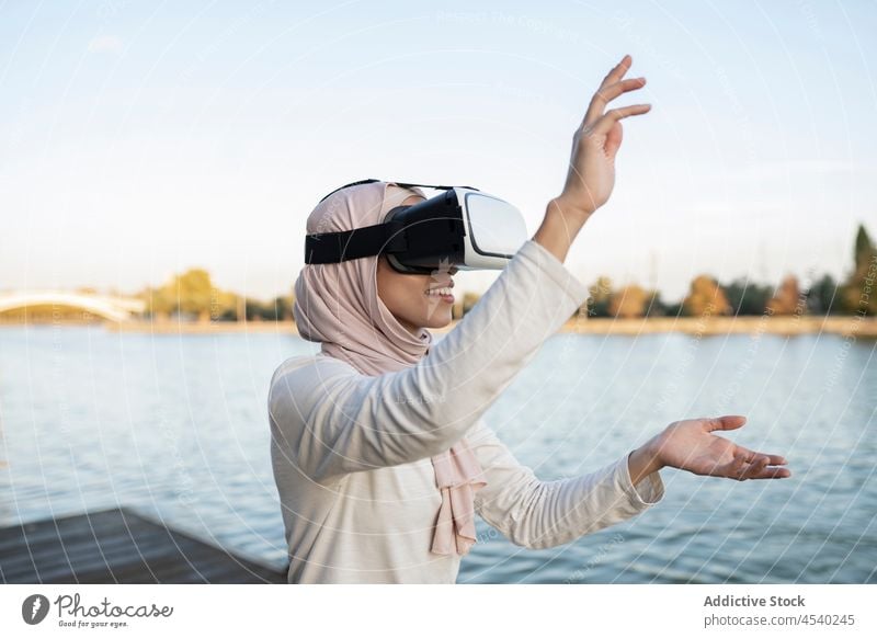 Arabische Frau mit VR-Headset an der Uferböschung Schutzbrille Virtuelle Realität Stauanlage Fluss simulieren Cyberspace Wasser arabisch muslimisch Hafengebiet