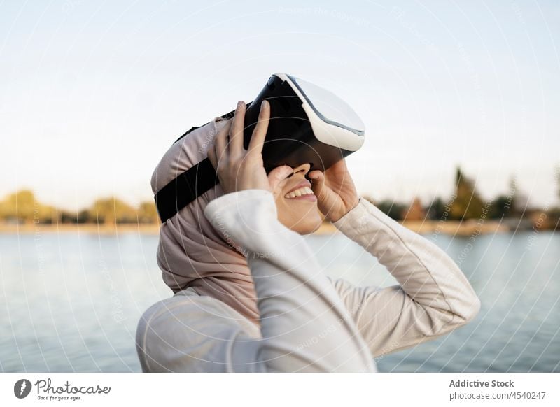 Arabische Frau mit VR-Headset an der Uferböschung Schutzbrille Virtuelle Realität Stauanlage Fluss simulieren Cyberspace Wasser arabisch muslimisch Hafengebiet