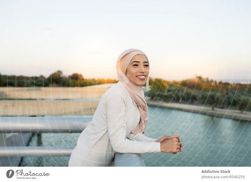 Positive arabische Frau auf dem Damm Hafengebiet Stauanlage Hijab Fluss Wasser Freizeit Zeitvertreib Flussufer Ufer Reling muslimisch Dame Sommer Zaun Lächeln