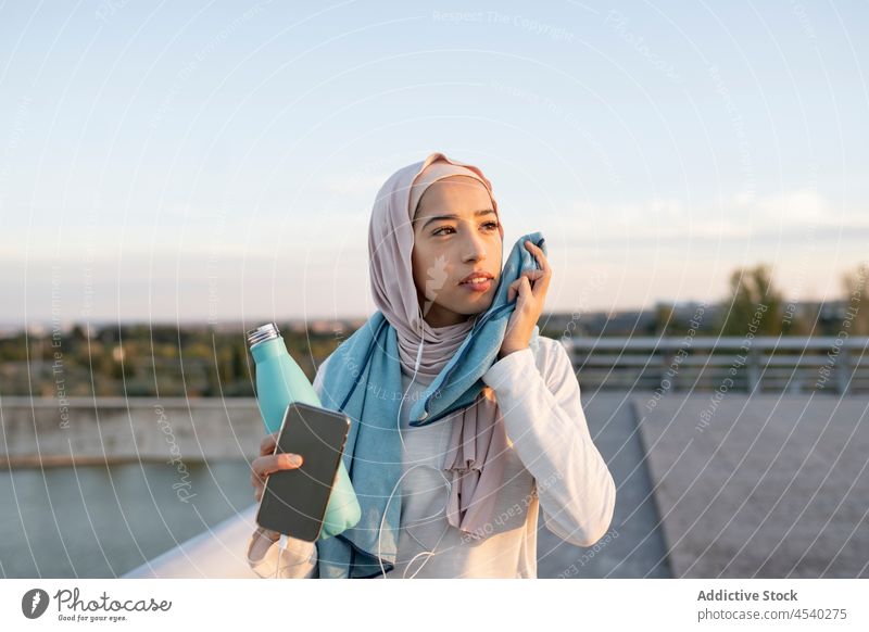 Müde arabische Frau wischt sich nach dem Training das Gesicht mit einem Handtuch ab müde Schweiß Wischen zuhören Musik benutzend Kopfhörer Smartphone muslimisch