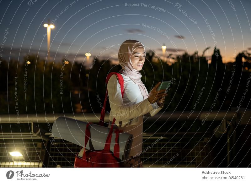 Lächelnde arabische Frau, die nach einem Training im Freien ein Handy benutzt Smartphone benutzend dunkel Sonnenuntergang Fitness Unterlage Nachricht muslimisch