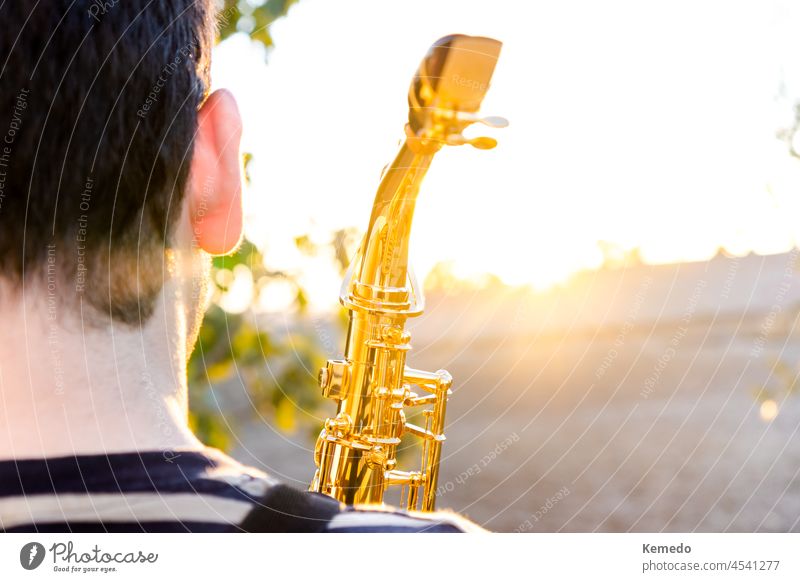 Mann hält ein Saxophon während eines Sonnenuntergangs in der freien Natur. Textfreiraum sonnig Sonnenlicht Saxophonist Musik Musikinstrument spielen Musiker