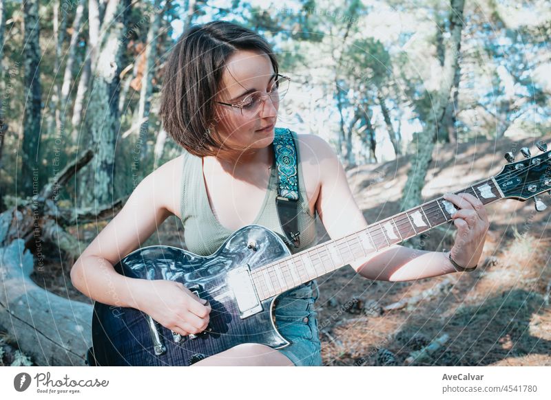 Junge Hipster Frau spielt die Gitarre außerhalb des Waldes Park der Stadt. Mit Spaß lernen eine neue Fähigkeit, Musik spielen saisonalen Stil. Junge kurze Haare Mädchen. Kopieren Raum