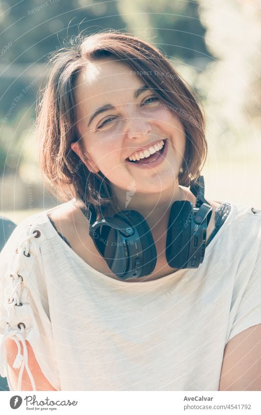 Junge Frau mit kurzen Haaren, die sich amüsiert, während sie einen großen Kopfhörer benutzt, um Musik zu hören. Aktivitäten im Freien. Glückliches junges Mädchen Musik genießen.